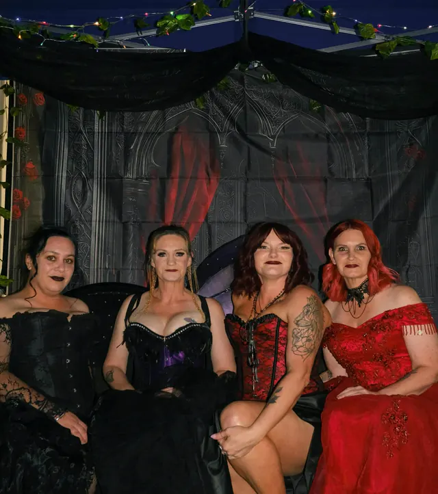 Four guests in corsets and ball gowns posed together on a couch in the gothic photo booth, under draped black netting and fairy lights