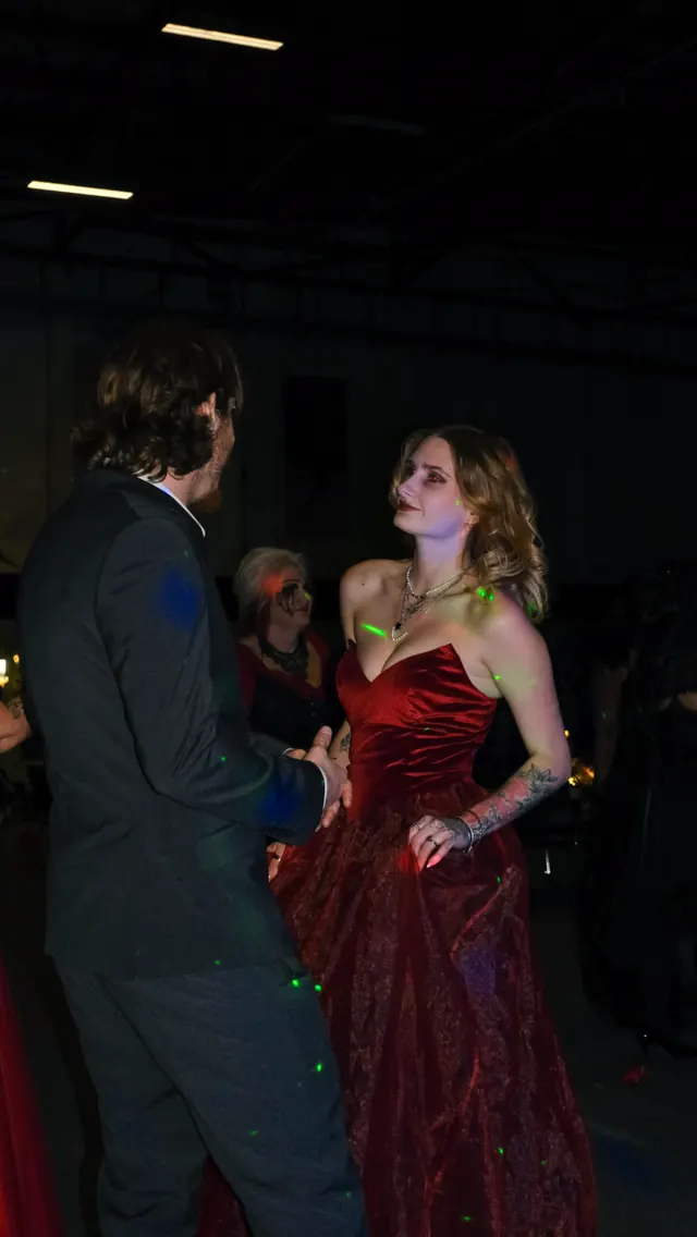 A guest in a red satin gown dancing with a partner in black tie under green laser light at the ball