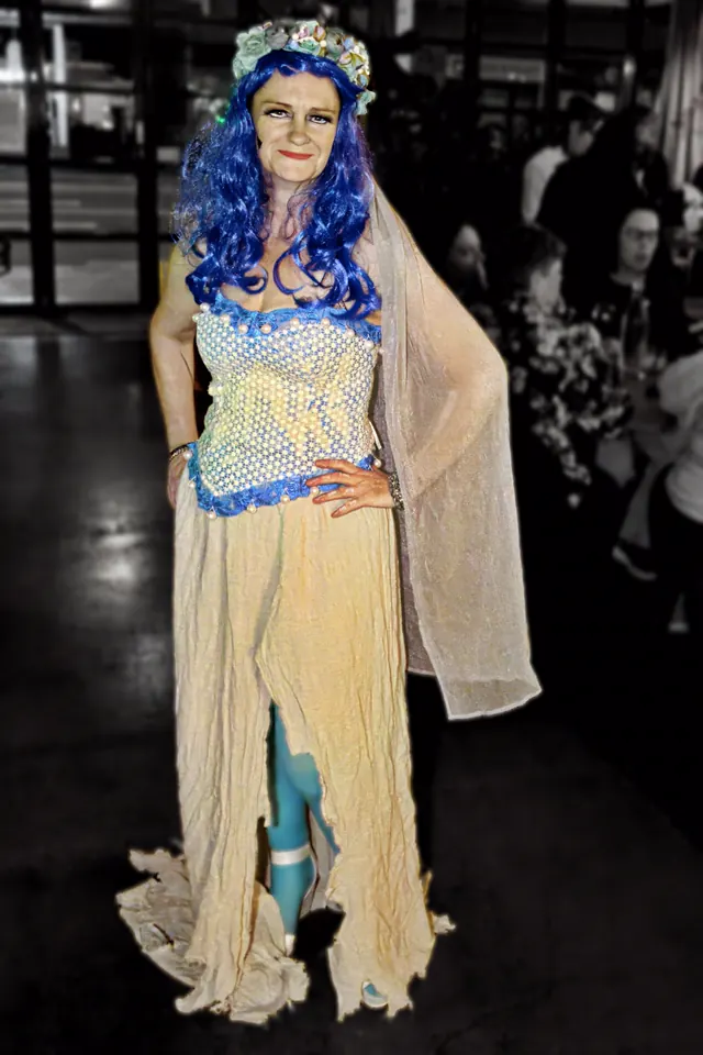 A guest dressed as a drowned bride in a torn cream gown, blue wig and a crown of shells, picked out in colour against a black and white room