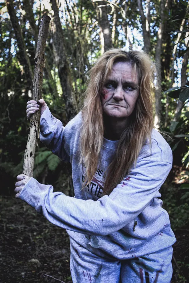 The Slitmore Institution patient gripping a broken branch like a weapon in daylight bush
