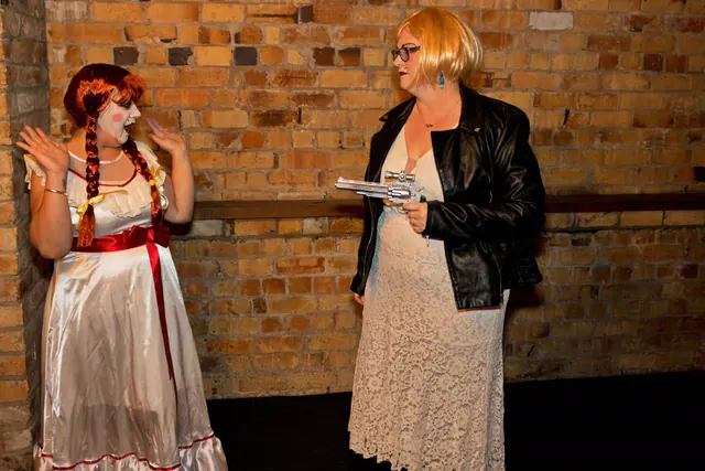 Two quiz night guests act out a scene against a brick wall - one dressed as a porcelain doll, the other in a leather jacket levelling a toy revolver at her