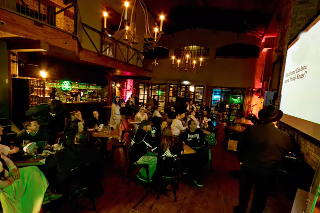 The full quiz night room under chandeliers and red light, every table taken, a question about Freddy Krueger up on the screen