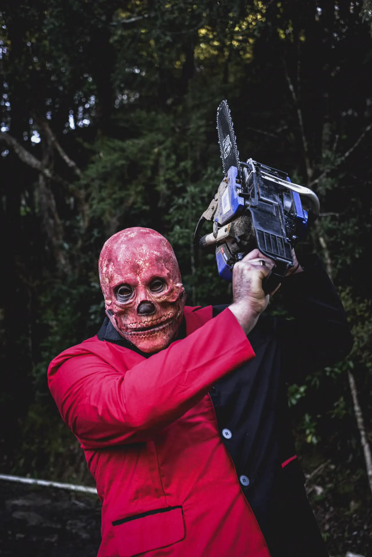 The red skull-masked performer swinging a chainsaw above his head on a bush track