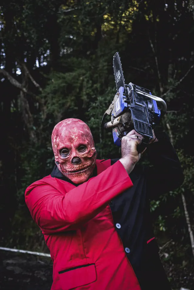 The red skull-masked performer swinging a chainsaw above his head on a bush track